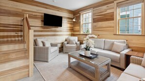 A modern log cabin interior with a sofa, chairs, a coffee table, and a TV mounted on the wall. - ‘Sand Swept’ - Downtown Private Cottage (Charleston)