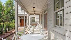 A covered patio with a round table and white chairs, a ceiling fan, and a lantern. - ‘Sand Swept’ - Downtown Private Cottage (Charleston)