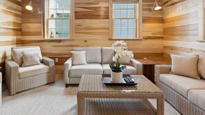 A cozy log cabin interior with a sofa, two armchairs, a coffee table, and two windows with blinds. - ‘Sand Swept’ - Downtown Private Cottage (Charleston)