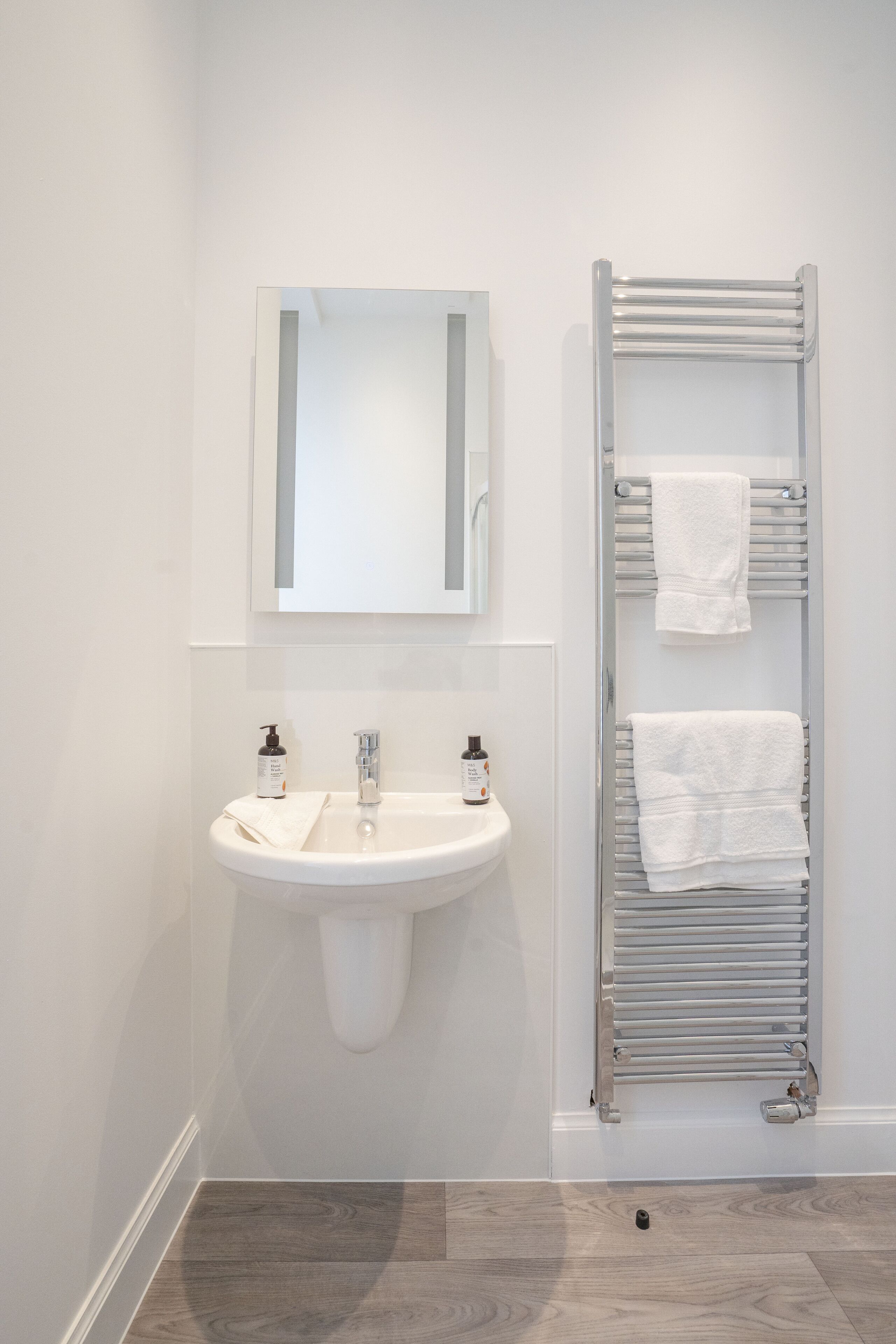 Un baño con lavamanos blanco, espejo y toallero.