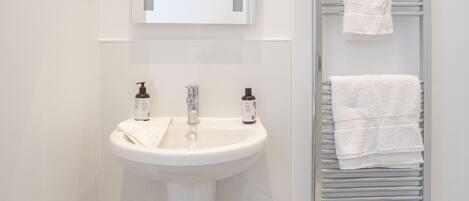 Un baño con lavamanos blanco, espejo y toallero.