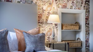 Een opgemaakt bed met kussens, een bedlampje en een klein plankje met manden, tegen een behangwand.