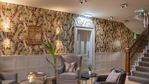 Een gezellige woonkamer met behang met een patroon, een comfortabele fauteuil, een leren bank en een trap op de achtergrond.
