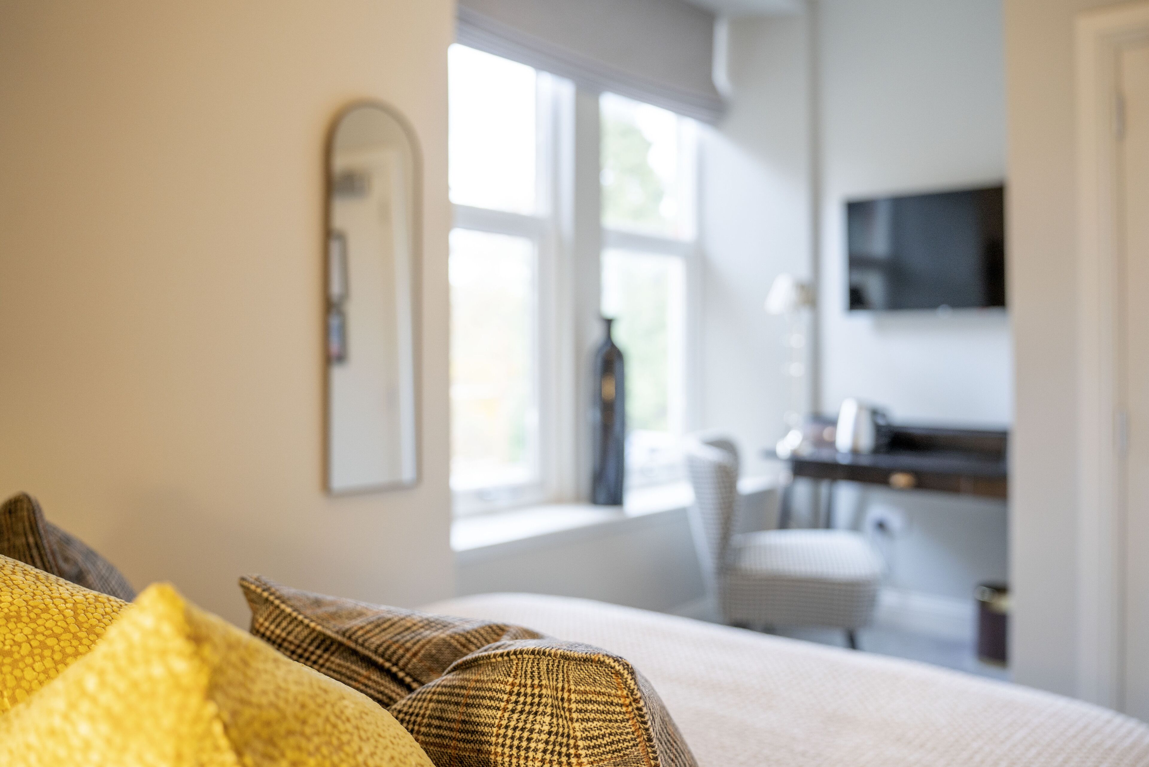 A bedroom with a bed, a television mounted on the wall, and a window providing natural light.