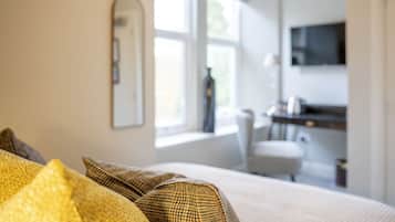 A bedroom with a bed, a television mounted on the wall, and a window providing natural light.