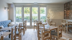 Een restaurant met houten tafels en stoelen, een blauwe met kussens beklede bank, en een citaat op de muur.
