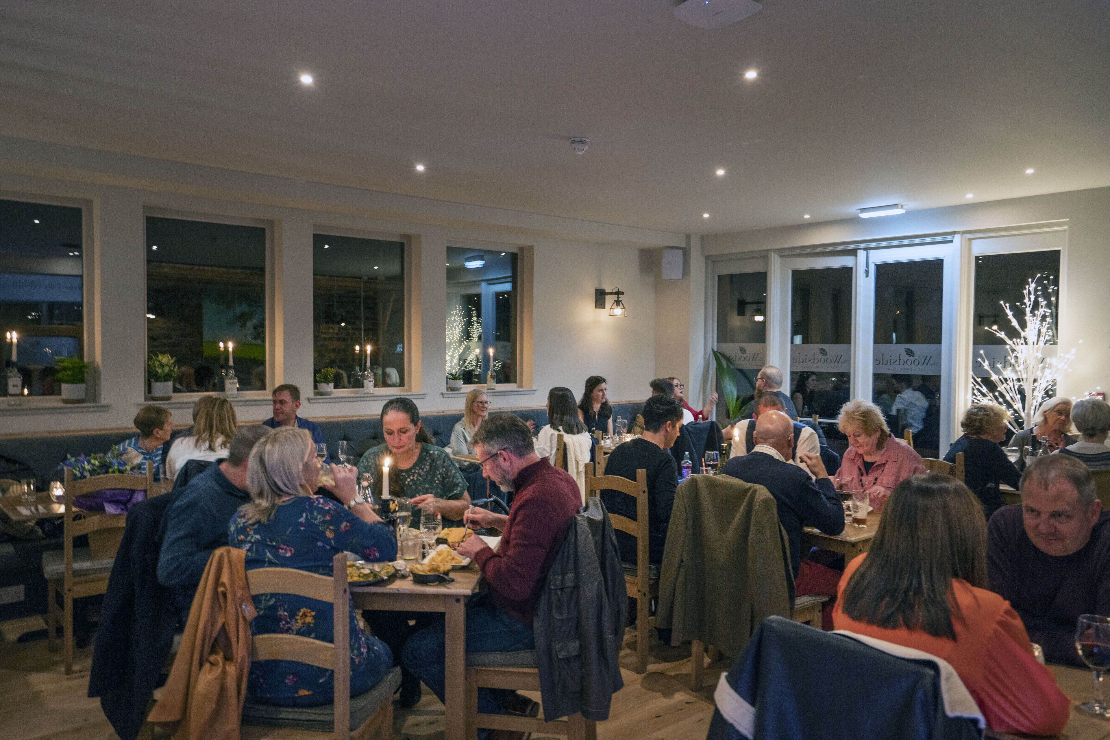 Un restaurante con varias mesas y sillas, ventanas amplias e iluminación interior.