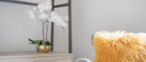 Een stoel met een zacht kussen, een houten bureau met lades en een vaas met witte bloemen.