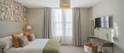 Une chambre à coucher avec un lit, un bureau, une chaise, un téléviseur et une fenêtre avec des rideaux.
