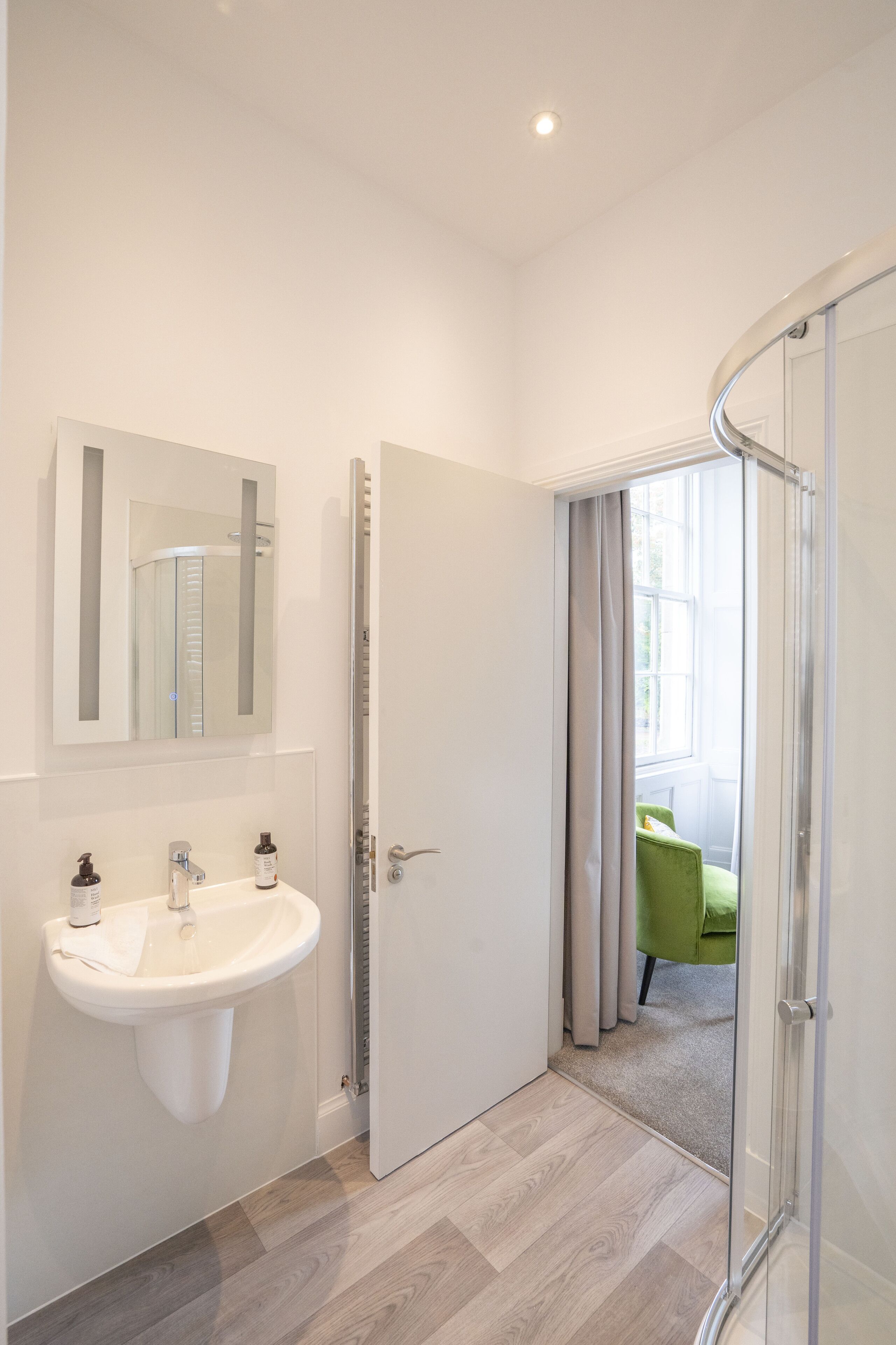 Un baño moderno con lavamanos blanco, espejo y cabina de ducha de vidrio.