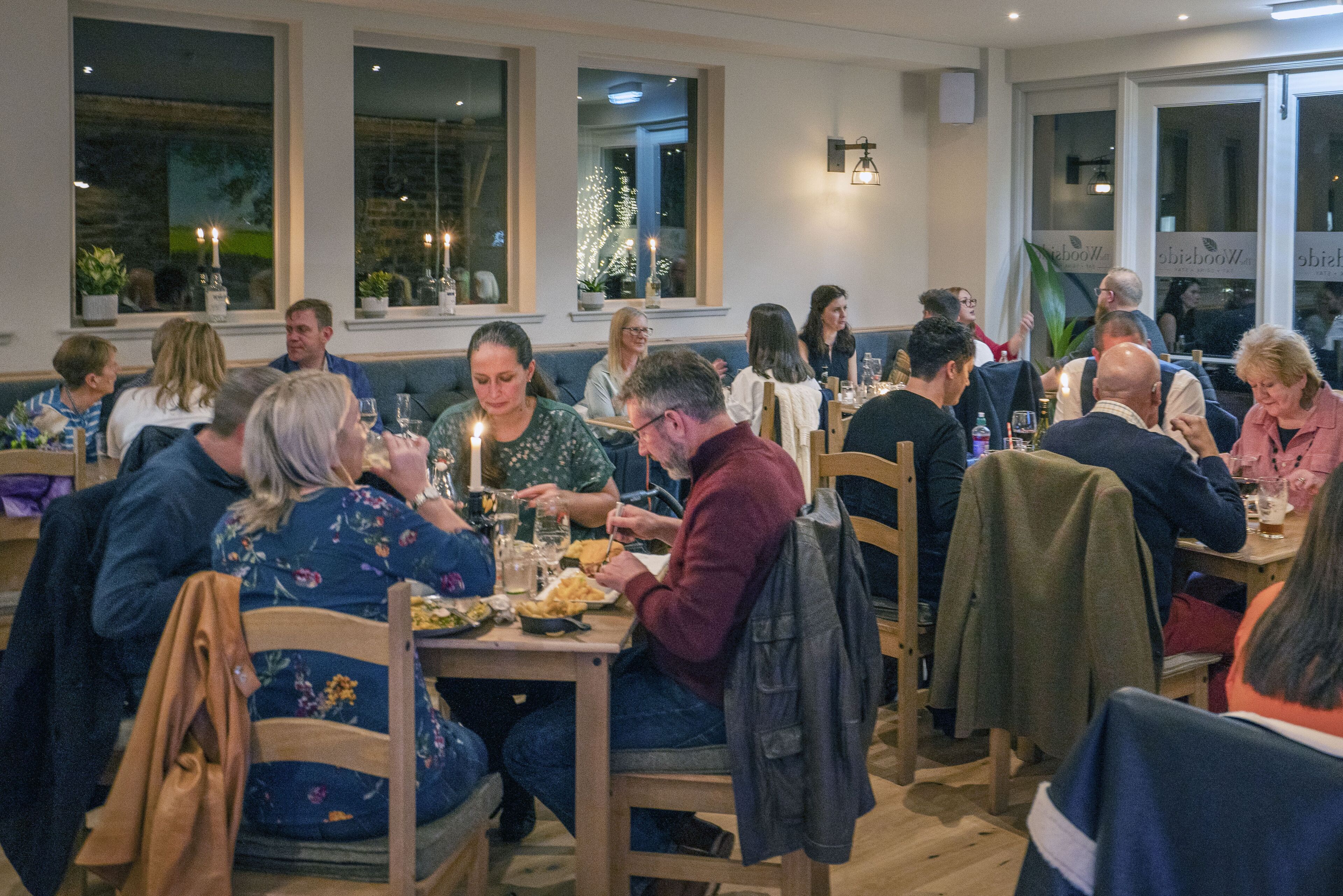 Un restaurante con mesas y sillas de madera, ventanas amplias y un ambiente acogedor.