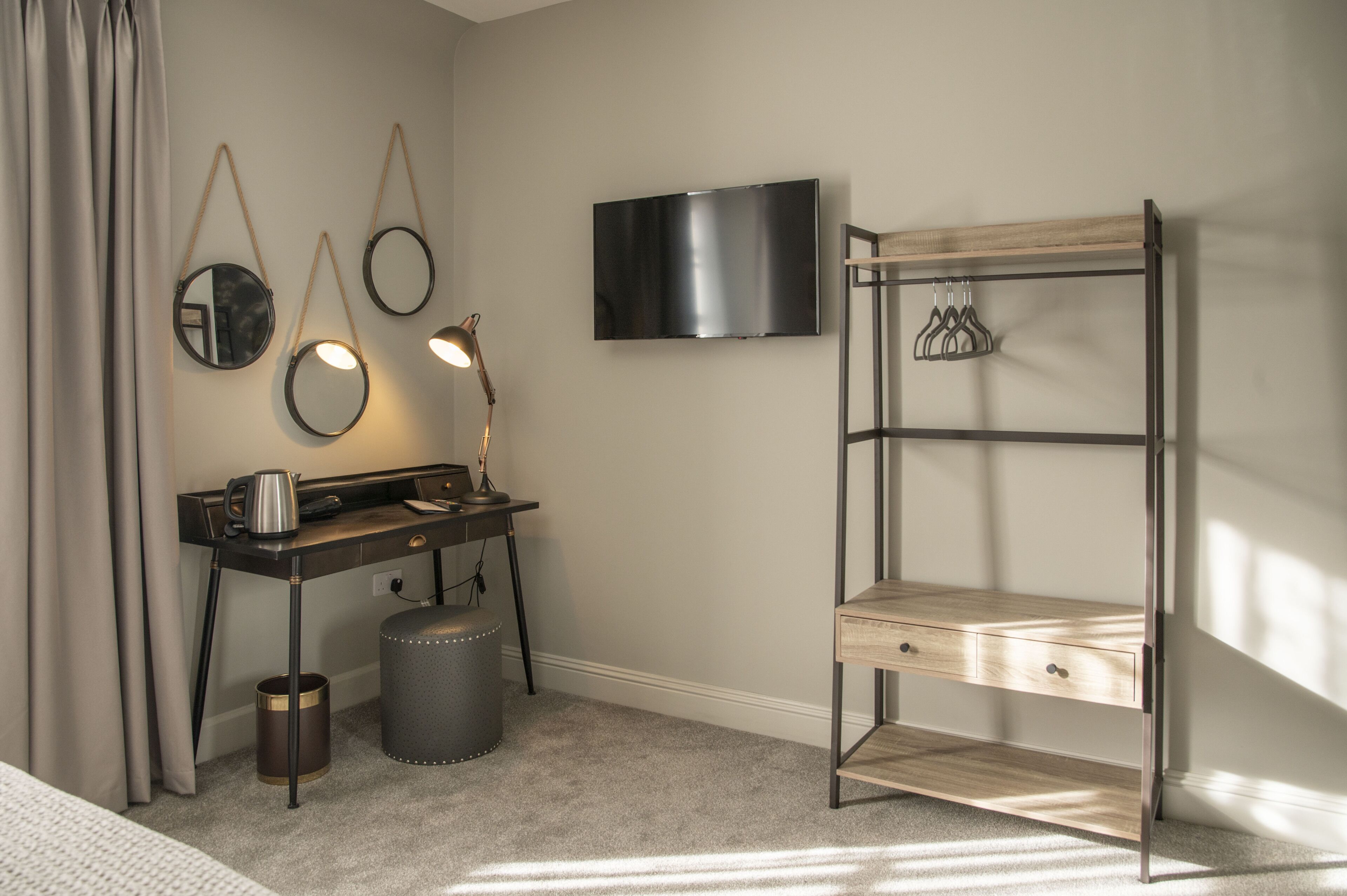 A hotel room with a desk, a TV, a mirror, and a wooden shelf.