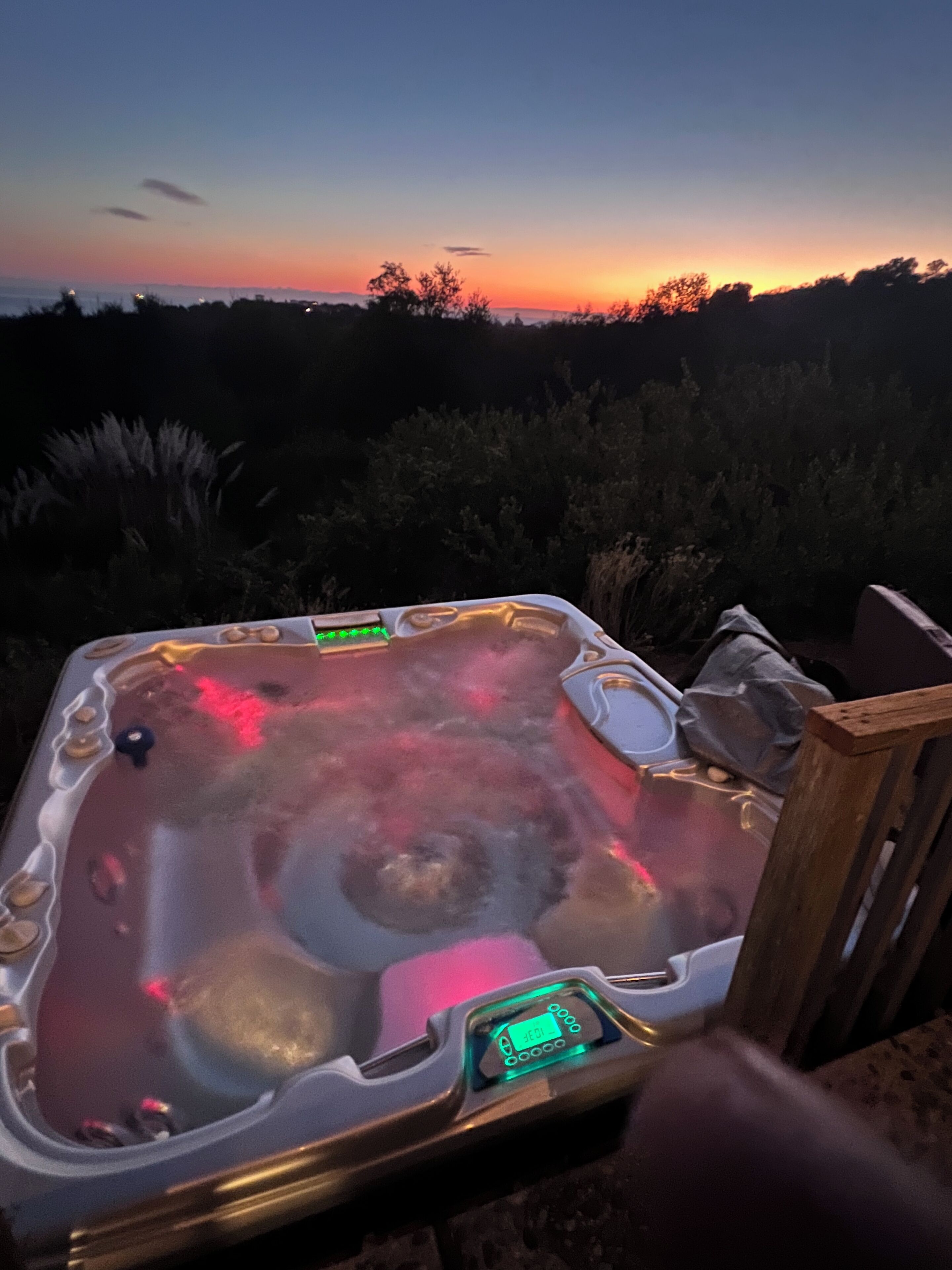 Ein Whirlpool mit digitaler Anzeige, umgeben von einer Holzterrasse und mit Blick auf einen Sonnenuntergang.