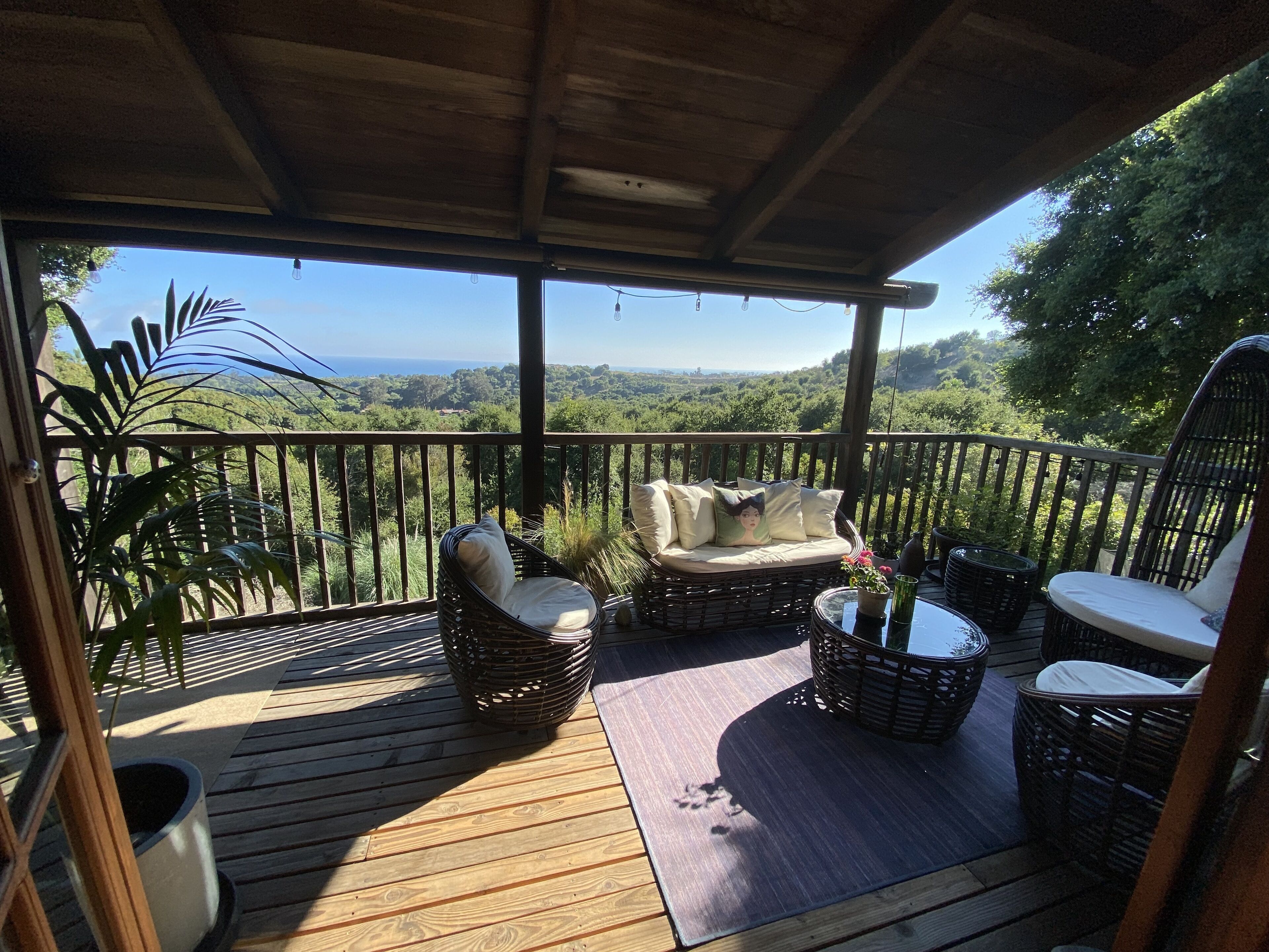 A wooden deck with wicker furniture, a cushioned bench, and a view of a forested landscape.