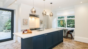 A modern kitchen with a large island, pendant lighting, and a view of the outdoors. - Springdale House (Buxton)