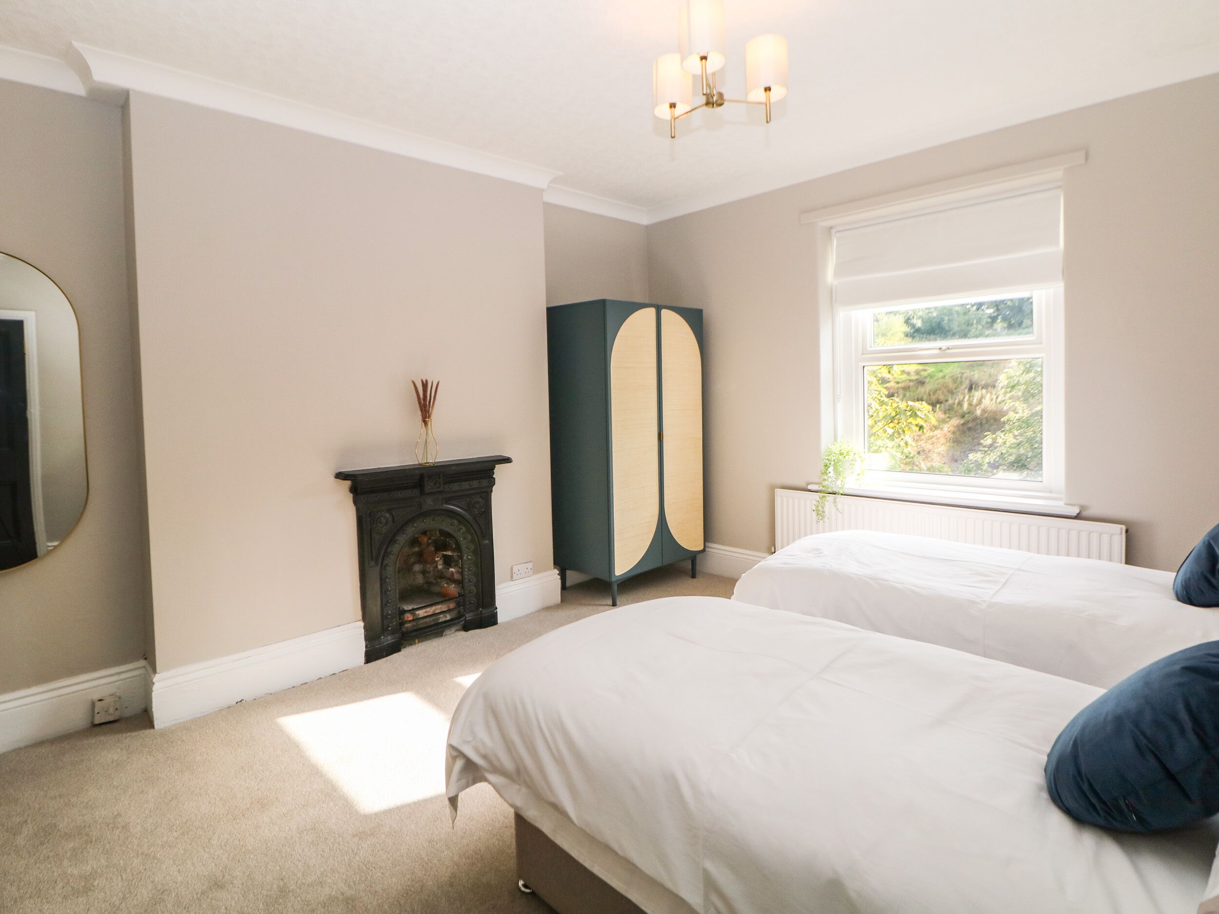 A bedroom with two beds, a fireplace, a wardrobe, and a window with a view.