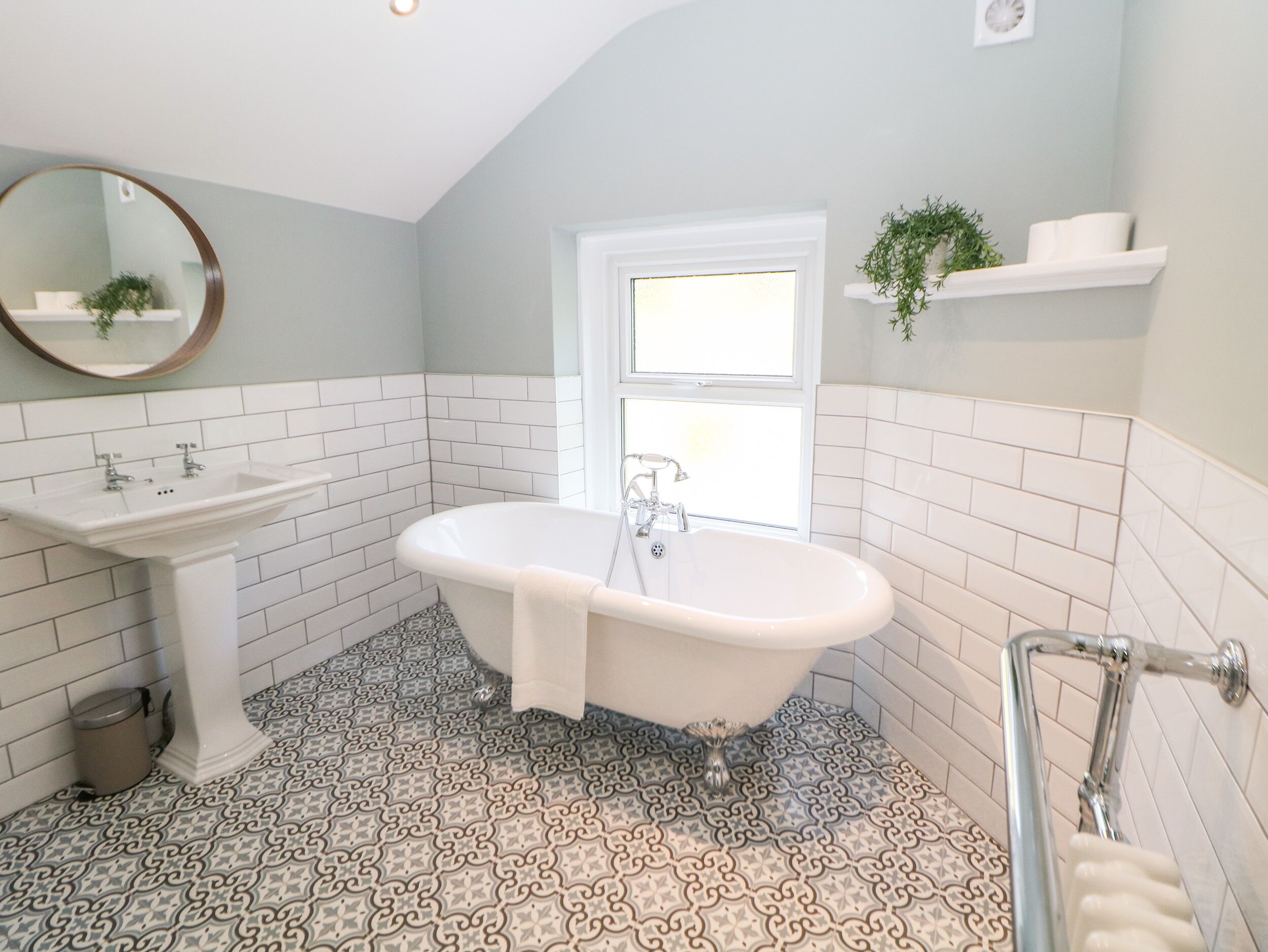 A bathroom with a freestanding bathtub, a pedestal sink, and patterned floor tiles.
