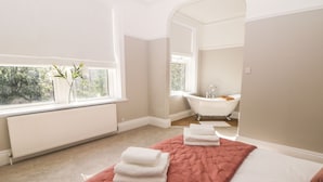 A bedroom with a bed, a window, a radiator, and a bathroom with a bathtub. - Springdale House (Buxton)