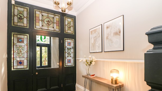 A black door with stained glass panels, a wooden bench with a vase of flowers, and two framed abstract paintings on the wall. - Springdale House (Buxton)