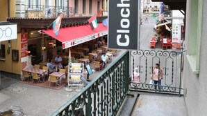 Un balcón con un cartel que dice "Clochard" que da a una calle con mesas al aire libre y un restaurante.