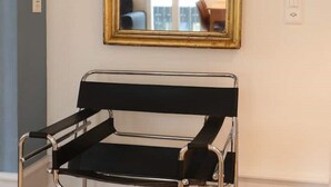Una habitación con una butaca de cuero negro, un espejo con marco dorado y suelo de madera.