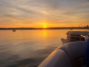 Een boot met uitzicht op de ondergaande zon boven een rustig meer, met andere boten in de verte.