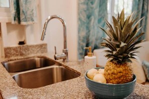 Una cocina con un lavamanos doble de acero inoxidable, un bol con piña y huevos, y un dispensador de jabón.