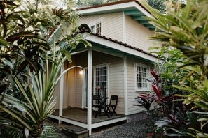 Una casa con porche, rodeada de plantas tropicales.
