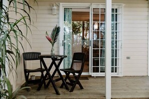 An outdoor seating area with a table and two chairs, a potted plant, and a sliding glass door leading to an interior space.