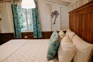 Un dormitorio con cama, cabecera de madera, ventana con cortinas y decoración de palmera montada en la pared.