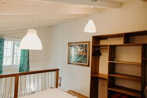 A room with a wooden bed, a white wall, a framed picture, and a wooden shelf unit.
