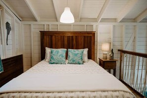 A bedroom with a wooden headboard, a bed with patterned bedding, a nightstand with a lamp, and a view of the outdoors.