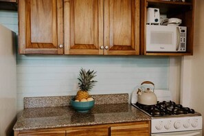 Una cocina con armarios de madera, encimera de granito, microondas, estufa a gas y un tazón de fruta.