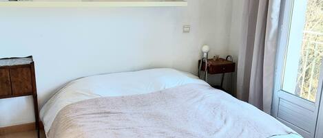 Un dormitorio con cama, mesita de noche, lámpara y una obra de arte en la pared.