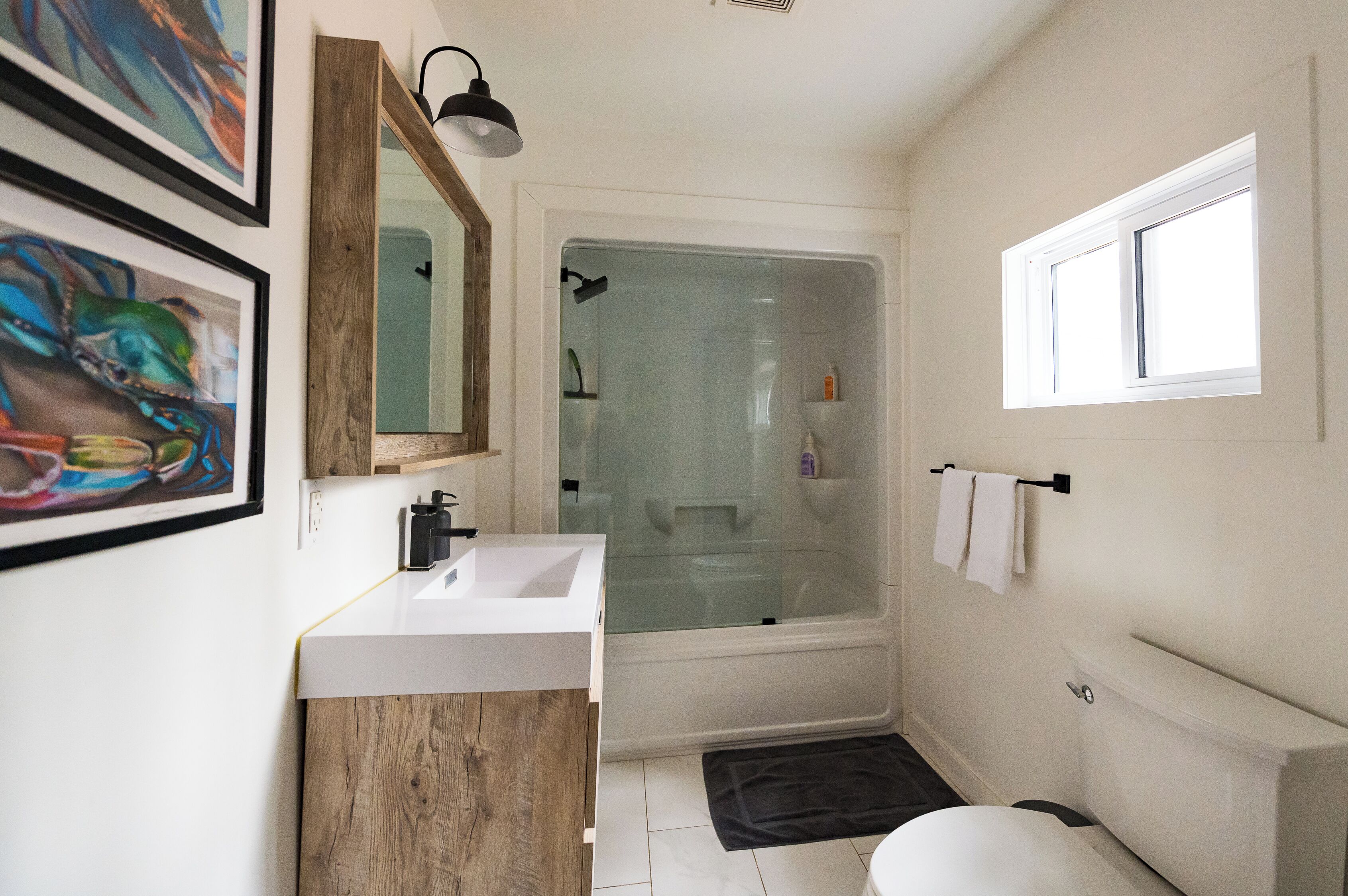 A bathroom with a white sink, wooden vanity, a glass shower enclosure, a toilet, and a window.