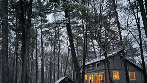 Une cabane nichée au cœur d’un paysage enneigé, entourée de grands arbres.
