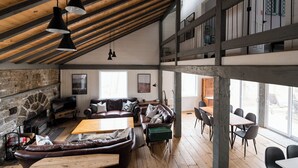 Un loft spacieux avec des poutres apparentes, une cheminée en pierre, des canapés en cuir et un coin repas doté d’un haut plafond.