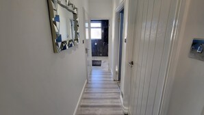 A hallway with a wooden floor, white walls, and a door with a handle. - Top Luxury 2 bed Apartment - London (London)