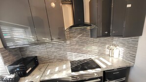 A modern kitchen with black cabinetry, a stainless steel range hood, a built-in oven, and a marble countertop. - Top Luxury 2 bed Apartment - London (London)