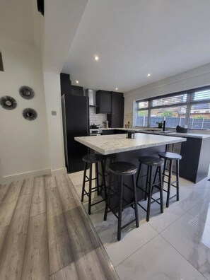 A modern kitchen with a central island, black bar stools, and a large window providing natural light. - Grand Exclusive 2 Bed Apartment - London (London)
