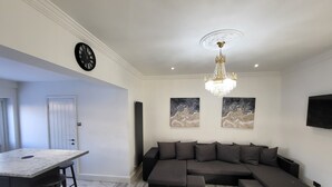 Un salon moderne avec un canapé d’angle, un îlot de cuisine en marbre et des œuvres d’art accrochées aux murs.