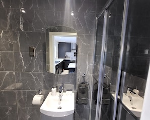 A modern bathroom with a marble backsplash, a sink with a mirror above it, and a glass shower enclosure. - Grand Exclusive 2 Bed Apartment - London (London)