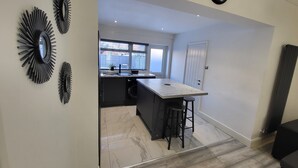 Une cuisine moderne avec un plan de travail en marbre, des tabourets de bar noirs et des œuvres d’art décoratives au mur.