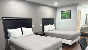 A hotel room with two beds, a desk, a chair, and a framed picture on the wall. - Bostonian Inn (New Boston)
