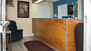 A reception area with a wooden counter, a blue chair, a dark blue armchair, and a brown rug. - Bostonian Inn (New Boston)