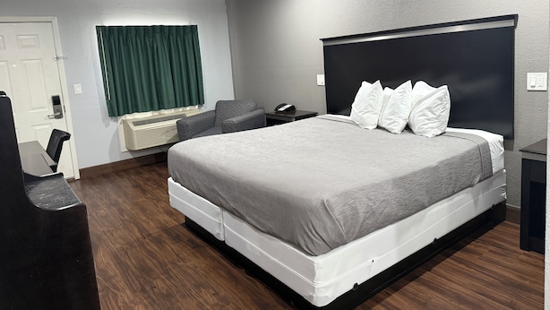 A modern hotel room with a large bed, a desk, a chair, a desk lamp, a telephone, and a window with curtains. - Bostonian Inn (New Boston)