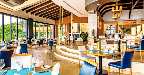 A spacious restaurant with high ceilings, large windows, and a mix of blue and white seating.