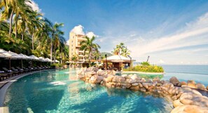 A resort pool with lounge chairs, palm trees, and a building with a dome roof.
