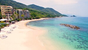 A beach with clear turquoise water, a sandy shore, and a hotel with multiple floors and balconies overlooking the beach. - 3 Bedroom Oceanfront Penthouse on the Beach (Puerto Vallarta)