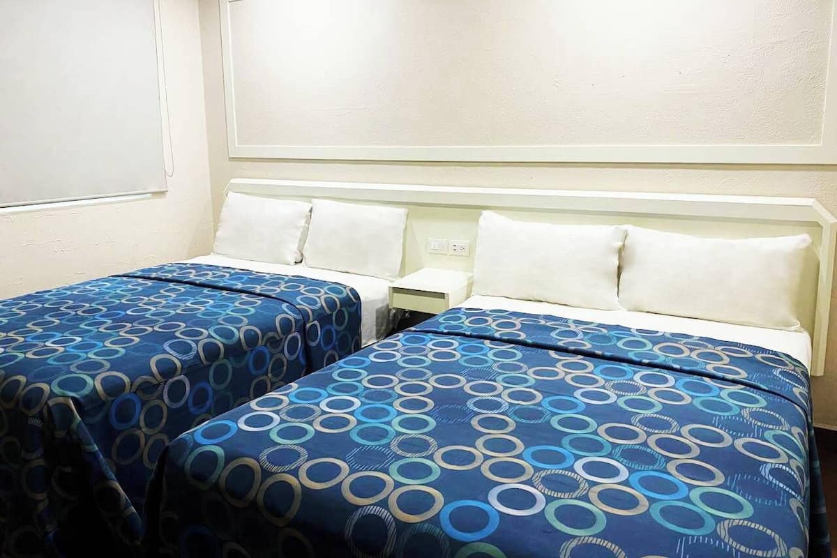 A hotel room with two single beds, each with a blue and white patterned bedspread.